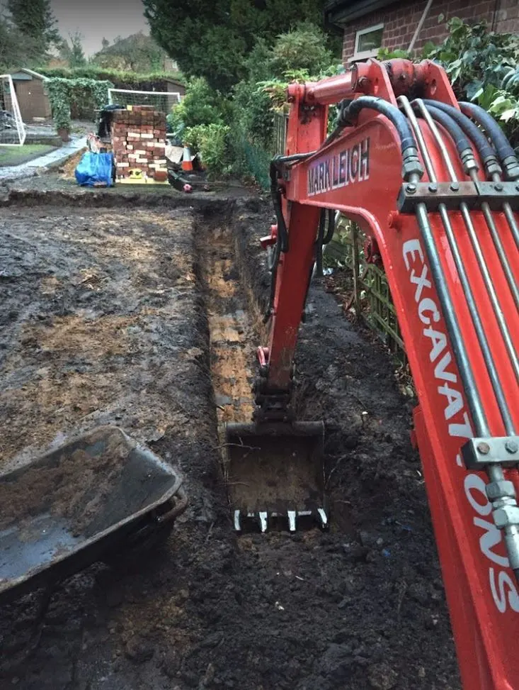 Excavator digging a narrow trench close to a house