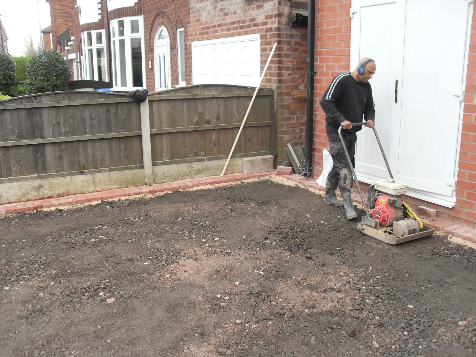 Groundworker compacting a driveway sub base with a plate compactor