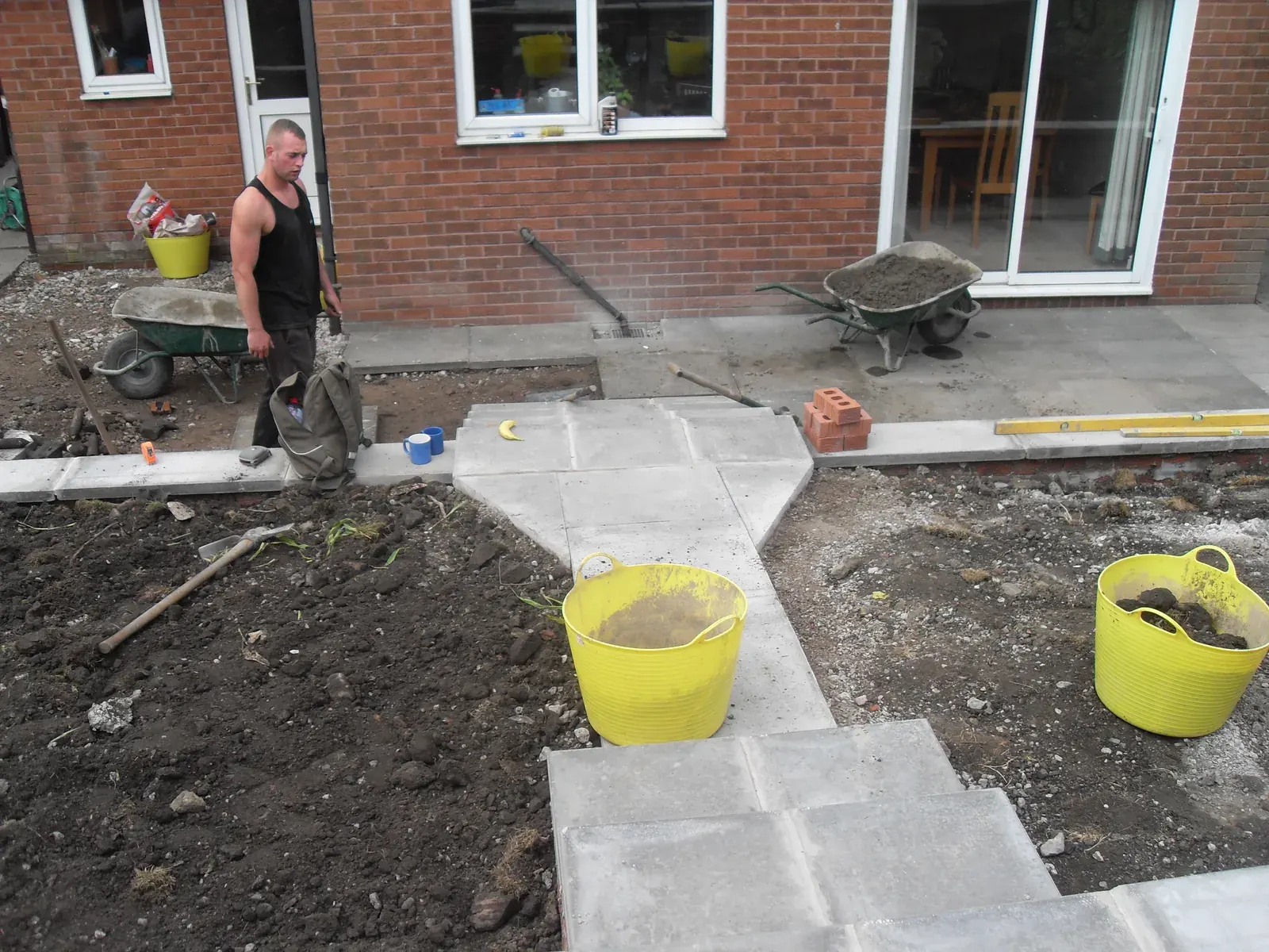 Groundworker laying a paved path alongside a house