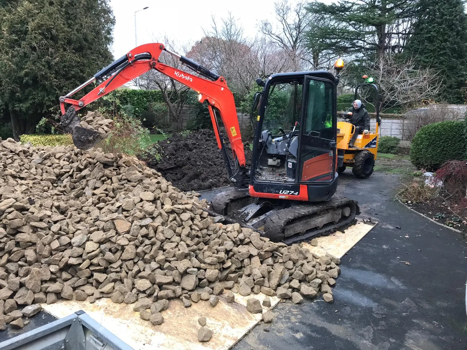 Mini excavator on a driveway job beside a pile of old block paving