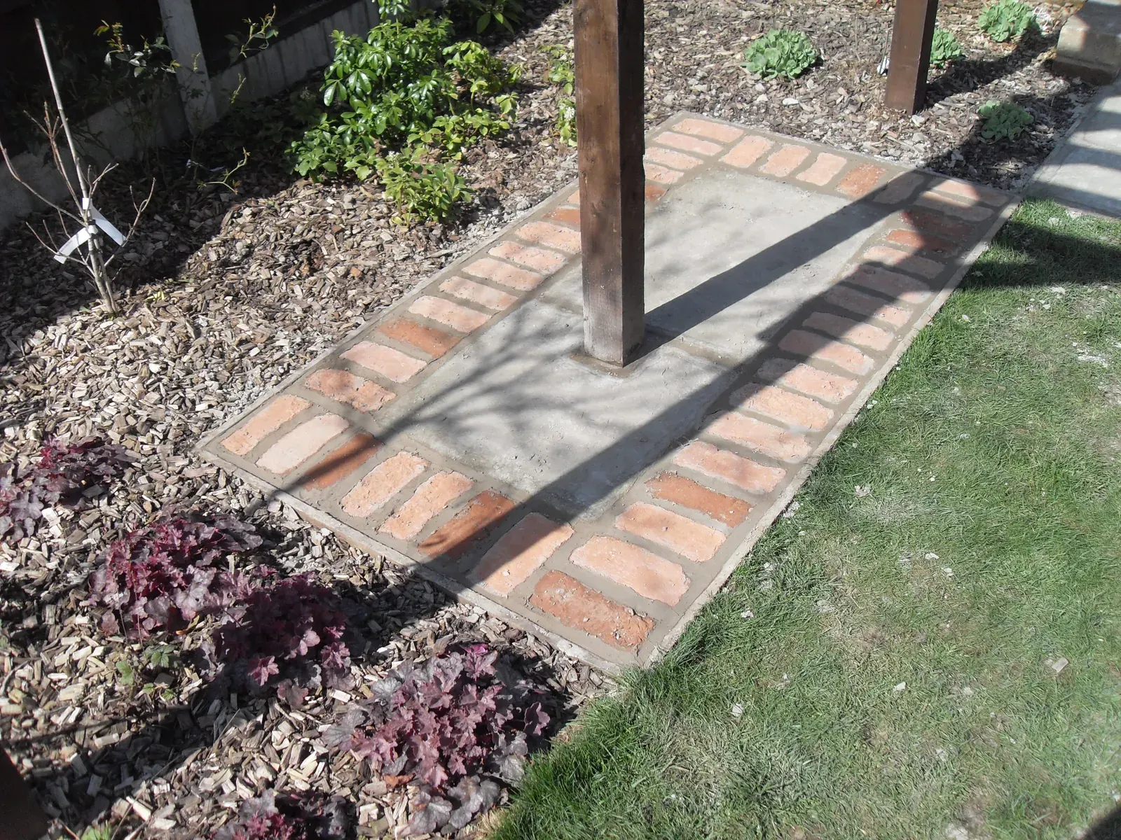 Paved path with brick edging laid around pergola posts