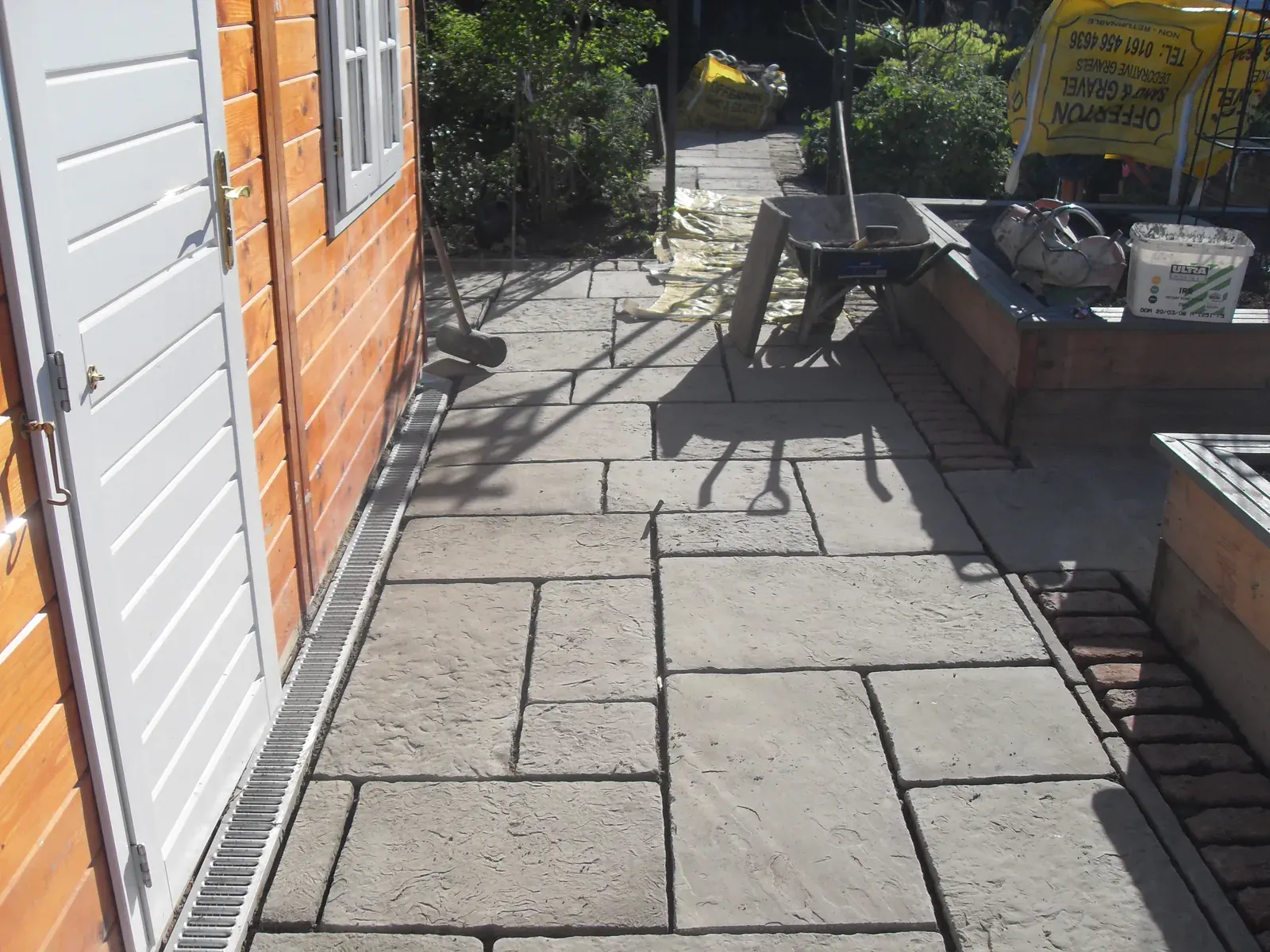 Sandstone patio laid out beside a garden shed and barbecue area