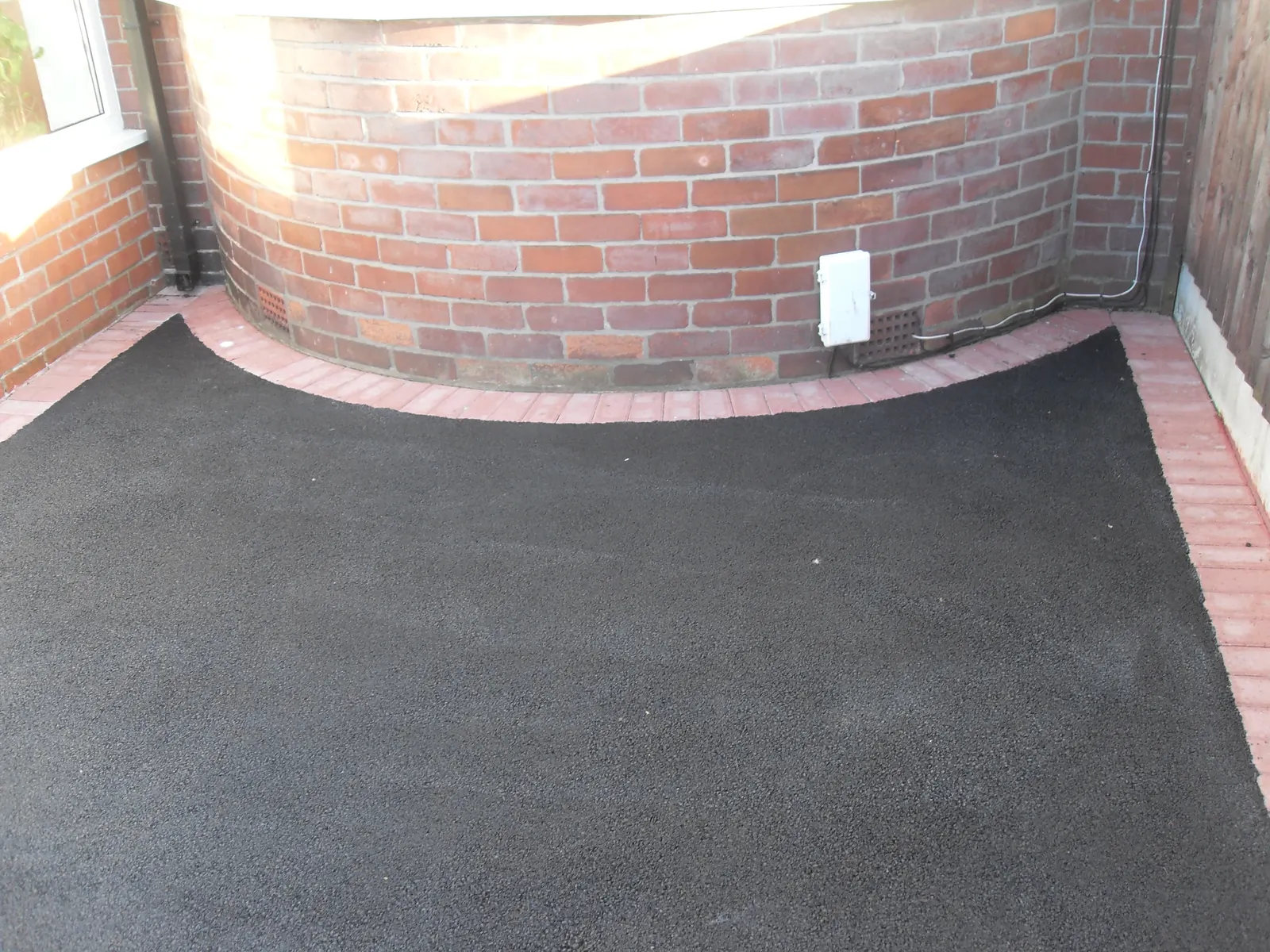 Tarmac driveway finished against a curved red brick wall
