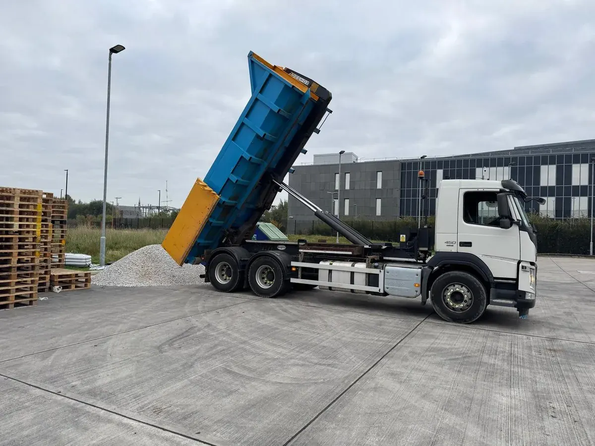 Tipper lorry discharging a roll-on-off skip body on a commercial yard