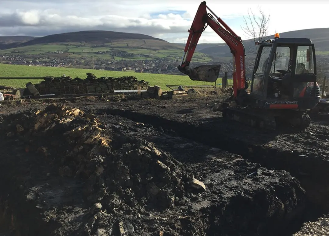 Tracked excavator stripping peat ground with the Pennine hills behind