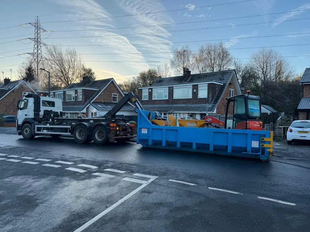 Two hook-lift skip lorries on a residential road at dusk